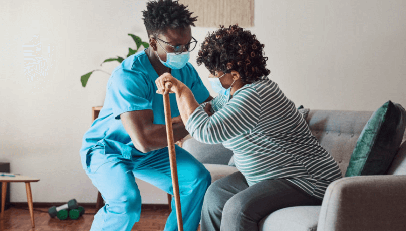 A caregiving wearing blue scrubs, helping a patient stand up