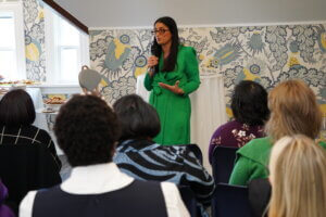 Dr. Mona Hanna-Attisha is wearing a green dress and glasses speaking in front of a group of women.