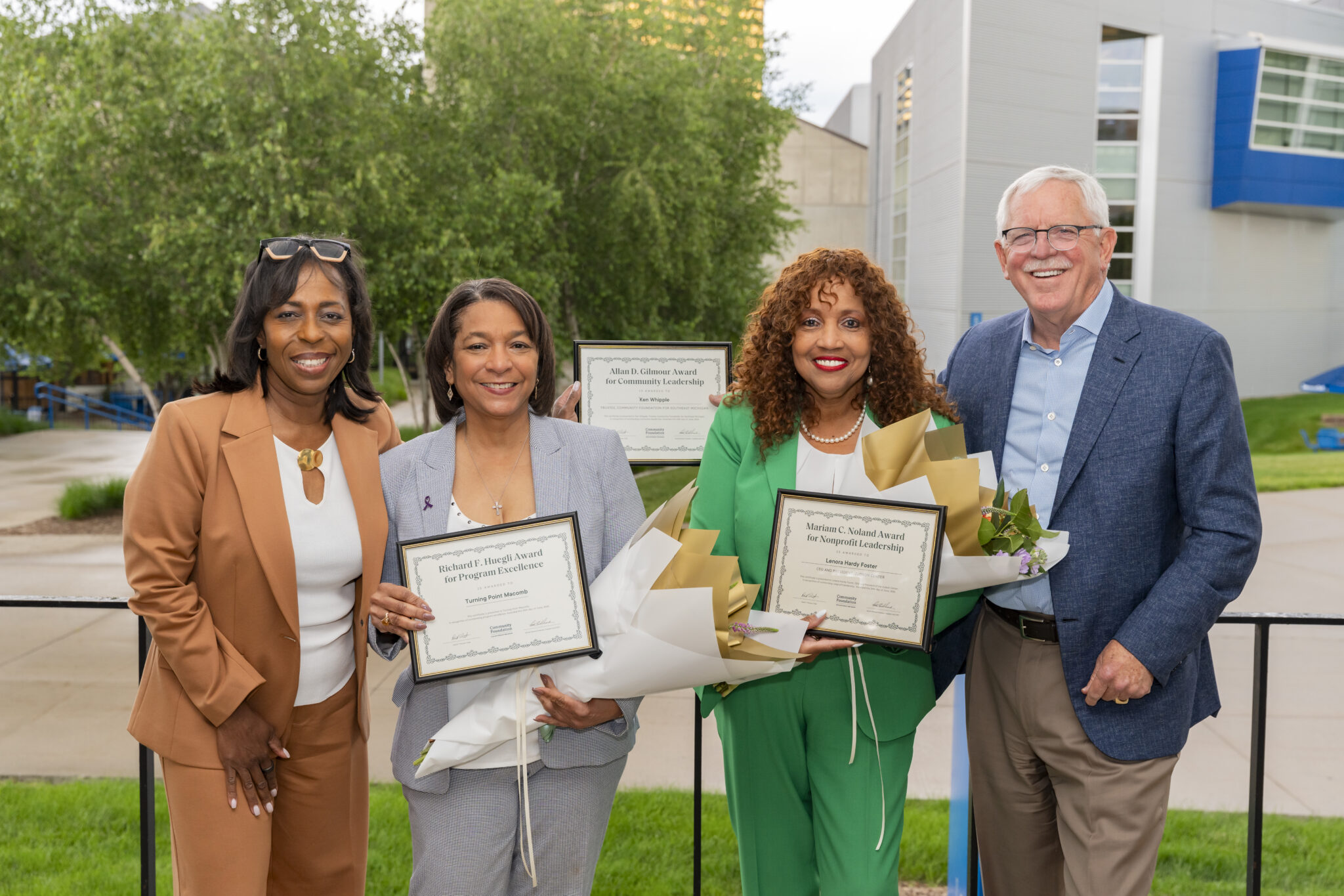 Several people smile while holding award certificates and flowers.
